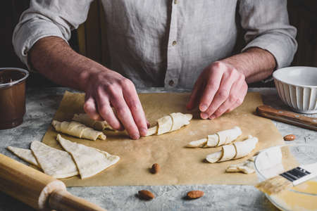 Homemade croissant preparing. Baker rolls the puff pastry stuffed with chopped almonds and hazelnut...