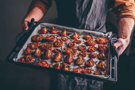 Baking Sheet Full of Freshly Oven Baked Tomatoes with Olive Oil and Thyme in a Male Handsの写真素材