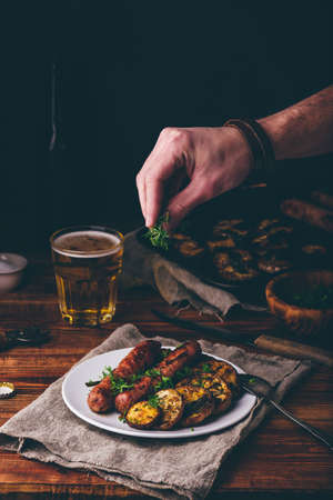 Pork Sausages Baked with Eggplant and Herbs on White Plate. Man Garnishing Meal with Dillの写真素材