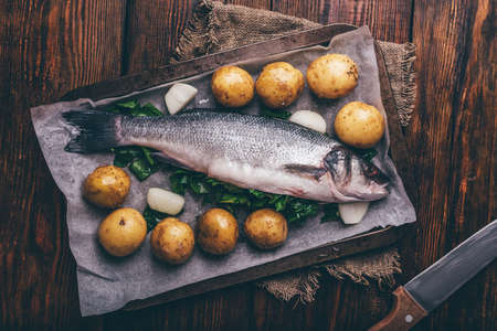 Fresh Sea Bass Stuffed with Sorrel on Baking Sheet Being Prepared with New Potatoes and Onion. View...