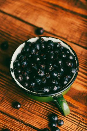 Green Cup Full of Purple Amelanchier Lamarckii Fruits on Rustic Wooden Surface. high angle view