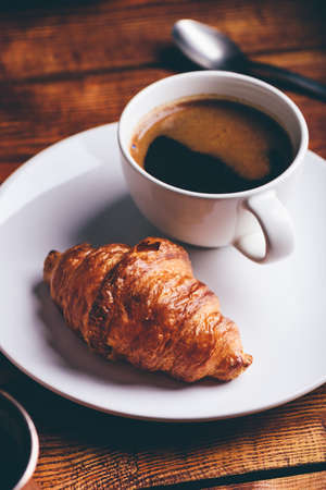 Cup of Black Coffee and Fresh Croissant on Rustic Tableの写真素材