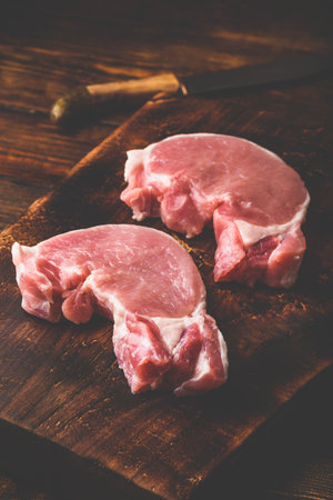 Two pork loin steaks with knife on rustic cutting boardの写真素材