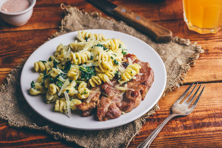 Pork Neck Steak with Creamy Spinach Pasta Garnished with Grated Parmesan Cheese on White Plateの写真素材