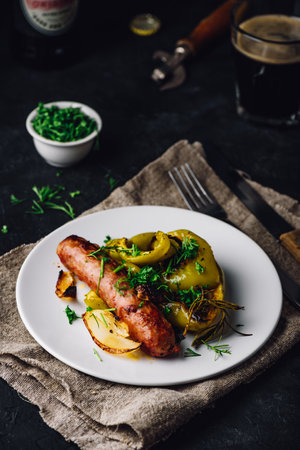 Pork sausage baked with bell peppers, onions and different herbs on white plateの写真素材