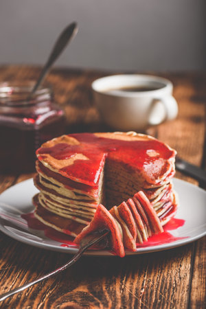 Stack of american pancakes with red berry jam on plate over rustic surfaceの写真素材