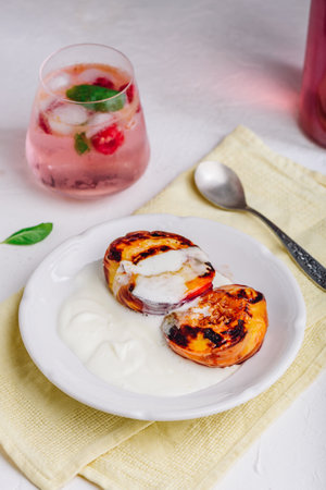 Served Oven Roasted Peaches with Honey and Whipped Heavy Cream on White Plate and Glass of Raspberry, Mint Mocktailの写真素材