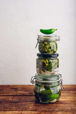 Three Glass Jars of Pickled Jalapeno Peppers with Herbs and Garlic on Wooden Table. Copy Spaceの写真素材