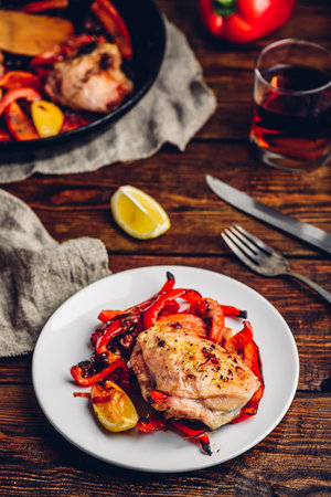 Oven baked chicken thighs with red bell peppers and lemon on white plate.の写真素材