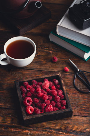 Cup of tea with raspberries and book on wooden table