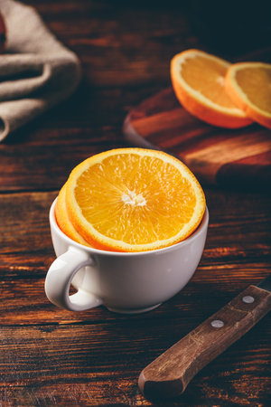 Sliced orange in a white cup on wooden surfaceの写真素材