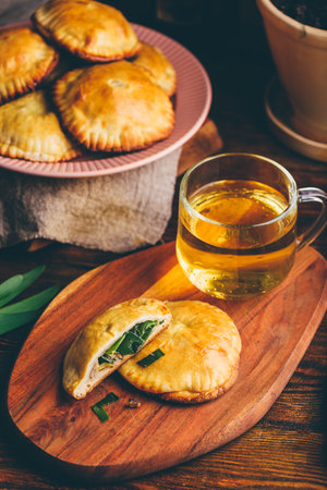 Oven Baked Pastries Stuffed with Siberian Chives and Mushrooms with Cup of Green Tea on Wooden Trayの写真素材