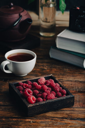 Raspberries in a wooden box and cup of tea on a wooden tableの写真素材