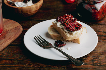 Toast with cream cheese and sundried tomatoes on white plateの写真素材