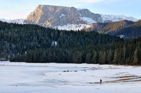 Mountain forest, hill, frozen lake and man
