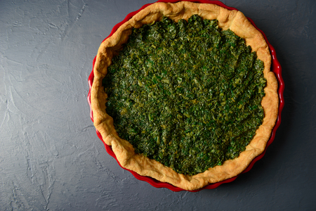 Close-up photo of baked tart dough with spinach in red ceramic tart pan, over gray textural surfaceの写真素材