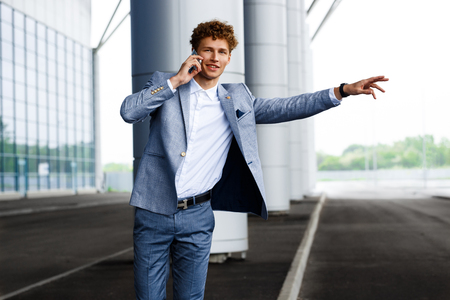 Picture of handsome young redhaired businessman catching the car and talking on phone looking at cameraの写真素材