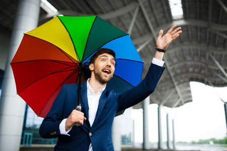 Picture of  young businessman holding motley umbrella and catching the carの写真素材