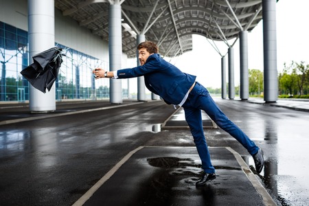 Picture of young businessman on street background holding broken umbrellaの写真素材