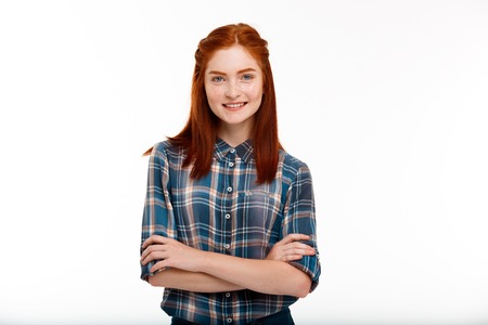 Portrait of young beautiful ginger girl looking at camera, smiling, arms crossed over white background. Copy space.の写真素材