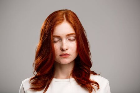 Portrait of young beautiful ginger girl with closed eyes over gray background.の写真素材