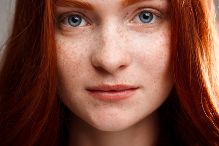 Close up portrait of young beautiful ginger girl looking at camera over gray background.の写真素材