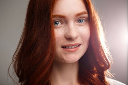 Portrait of young beautiful ginger girl smiling, looking at camera over gray background.の写真素材