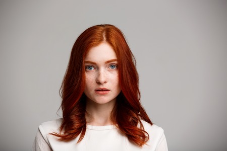 Portrait of young beautiful ginger girl looking at camera over gray background.の写真素材