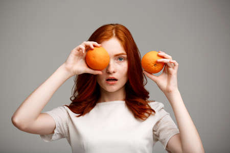Portrait of young beautiful ginger girl hiding eye with  orange, surprised, over gray background.の写真素材