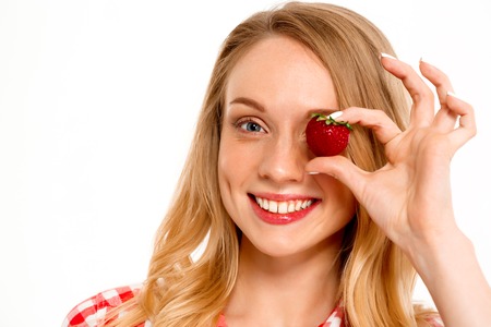 Portrait of young beautiful country girl with strawberry smiling, looking at camera over white background.の写真素材
