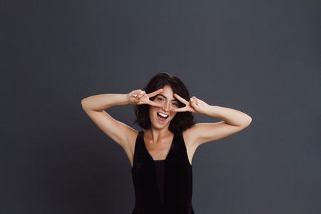 Beautiful young woman posing over grey background and make two peace funny gestureの写真素材
