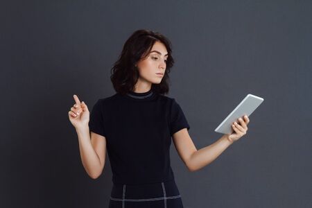 Young woman posing over grey background and holding tablet in hands