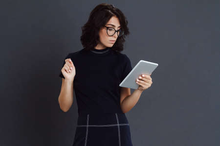 Young woman posing over grey background and holding tablet in handsの写真素材