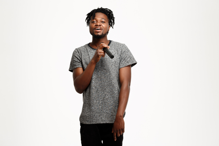 Young handsome african man looking at camera, singing in microphone over white background. Copy space.の写真素材