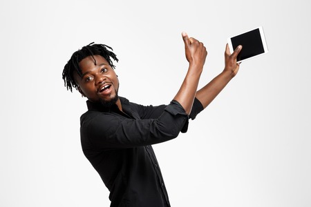 Young successful african businessman in black shirt making selfie, looking at camera over white background. Copy space.の写真素材
