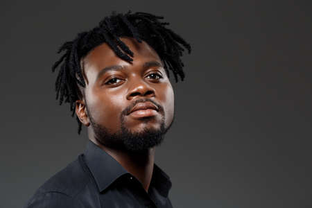 Young successful african businessman in black shirt posing, looking at camera over dark background. Copy space.の写真素材