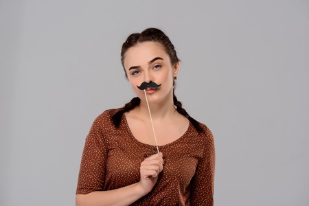 Young beautiful girl wearing fake mustache, looking at camera over purple background. Copy space.