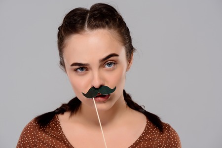 Young beautiful girl wearing fake mustache, looking at camera over purple background. Copy space.の写真素材