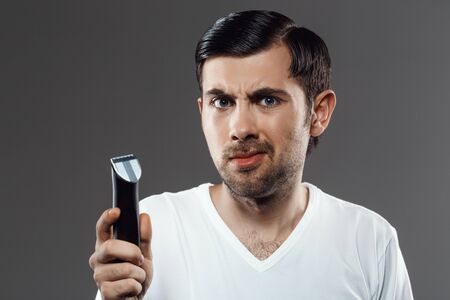 Young handsome man shaving with electric razor over grey background.の写真素材