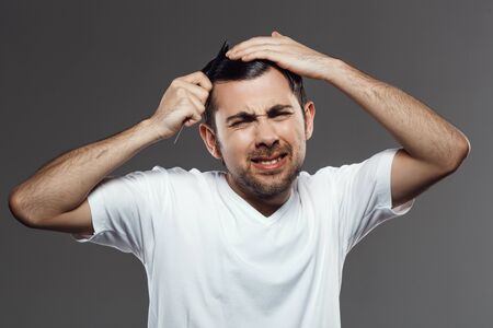 Upset young handsome man trying to comb hair over grey background.の写真素材