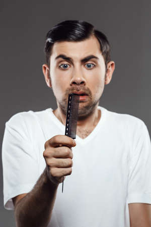 Young handsome man holding and looking at dirty comb over grey background.の写真素材