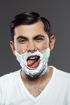 Young handsome man applying cream for shave on face over grey background.の写真素材