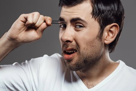 Young handsome man in white shirt tweezing eyebrows over grey background.の写真素材