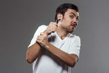 Young handsome man fighting with shaver over grey background. Copy space.の写真素材