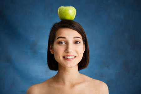 Picture of tender young girl holding apple over blue background