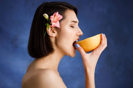 Picture of tender young girl eating orange over blue backgroundの写真素材