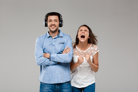 Young beautiful woman shouting, angering with man in headphones over grey background. Copy space.の写真素材