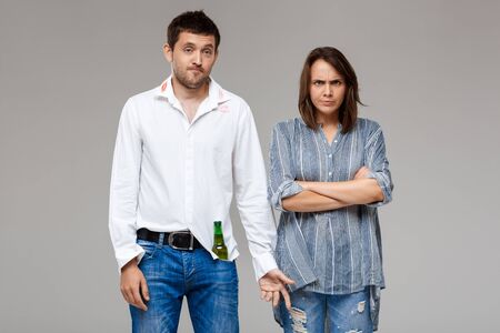 Young beautiful woman quarreling, angering with drunk husband over grey background. Copy space.の写真素材
