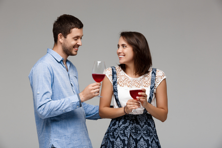 Young beautiful married couple drinking wine, smiling over grey background. Copy space.の写真素材