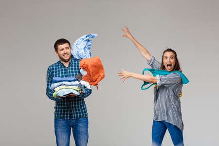 Young beautiful married couple holding wash clothes, looking at camera, fighting, shouting over grey background. Copy space.の写真素材